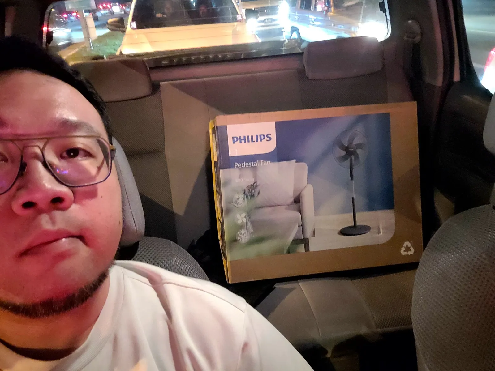Selfie in the car with a boxed standing fan in the back