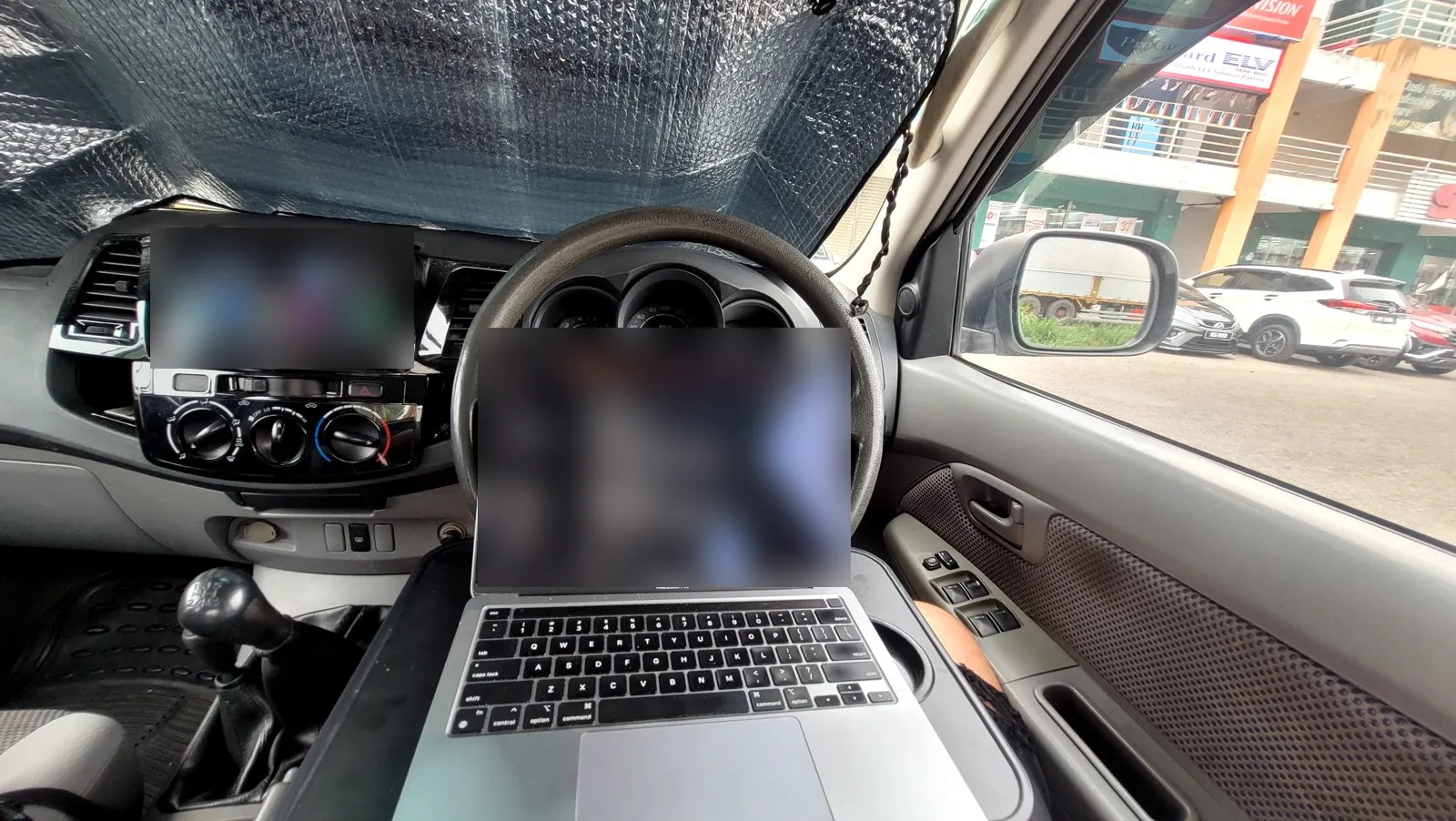 A laptop on the steering wheel of a pickup truck, screen blurred