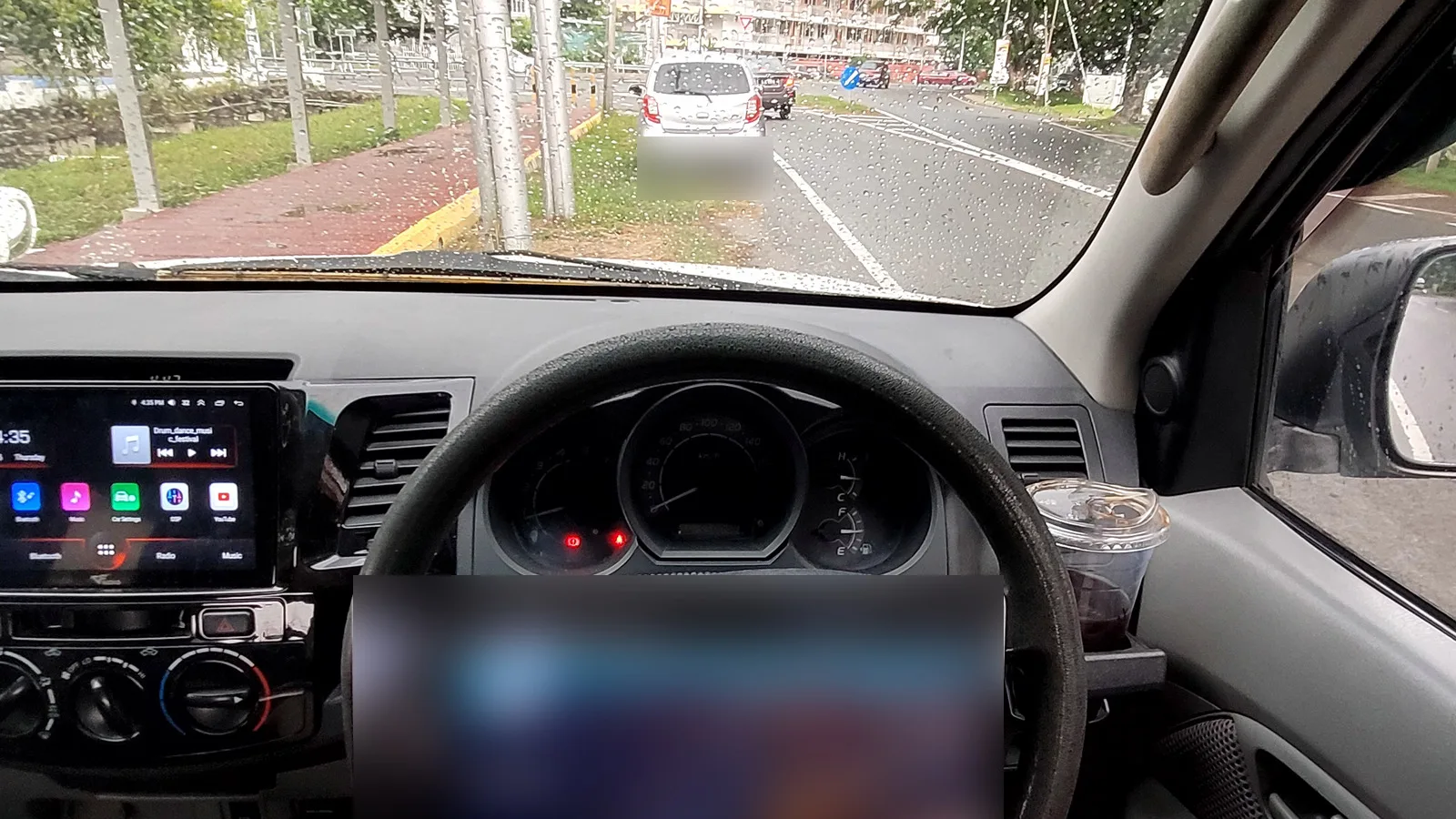A laptop on the steering wheel of a parked car, rain on the windscreen